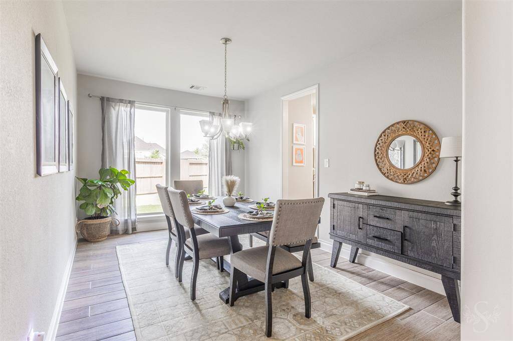 The elegant formal dining room is bathed in natural light from tall windows, creating an inviting space for entertaining. Stylish wood-look tile and a chic chandelier add warmth and sophistication to the room.