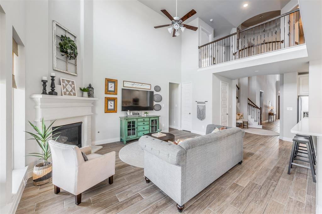 Soaring ceilings and an open second-floor balcony overlook the spacious family room, anchored by a timeless fireplace and mantel. The open-concept design flows effortlessly into the kitchen and entry.