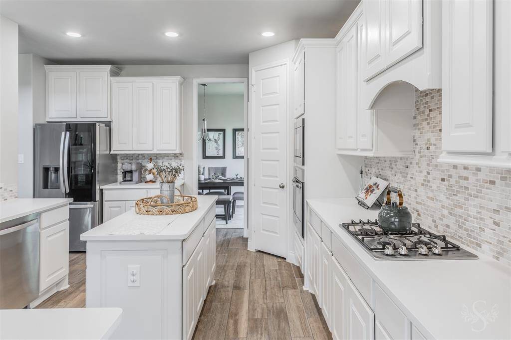 Crisp white cabinetry, modern backsplash, gas cooktop and sleek stainless steel appliances define this light and bright kitchen. A large center island adds prep space along with the miles of granite counters.
