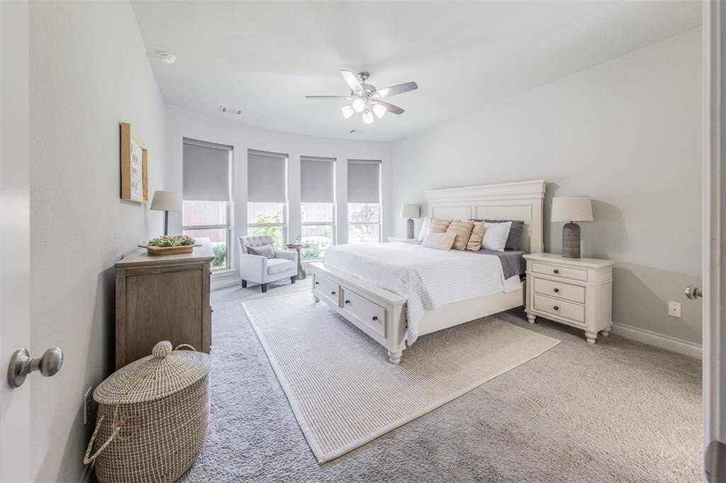 The spacious primary suite offers a peaceful retreat with a curved wall of windows with shades, soft carpet for comfort, and abundant natural light. Neutral tones and elegant finishes create a calm, inviting atmosphere.