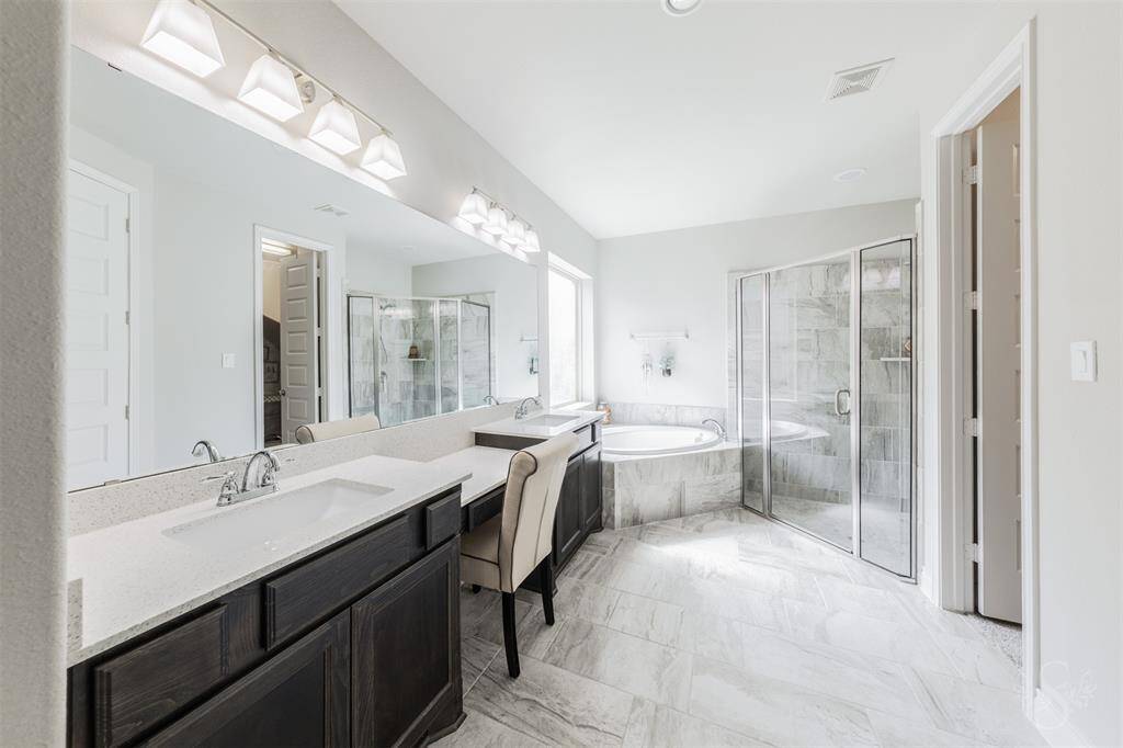 Indulge in spa-like luxury with dual vanities, a large soaking tub, and a glass-enclosed shower surrounded by elegant tile. A built-in makeup vanity and ample counter space enhance both function and comfort.