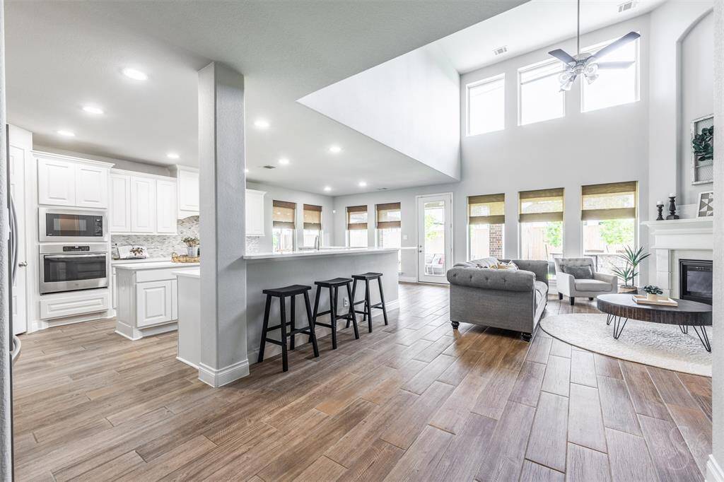 This light-filled living space boasts soaring ceilings, a wall of windows and beautiful wood-look tile flooring for seamless elegance. The open-concept design flows effortlessly into the kitchen and breakfast area, creating a perfect layout for modern living and entertaining.