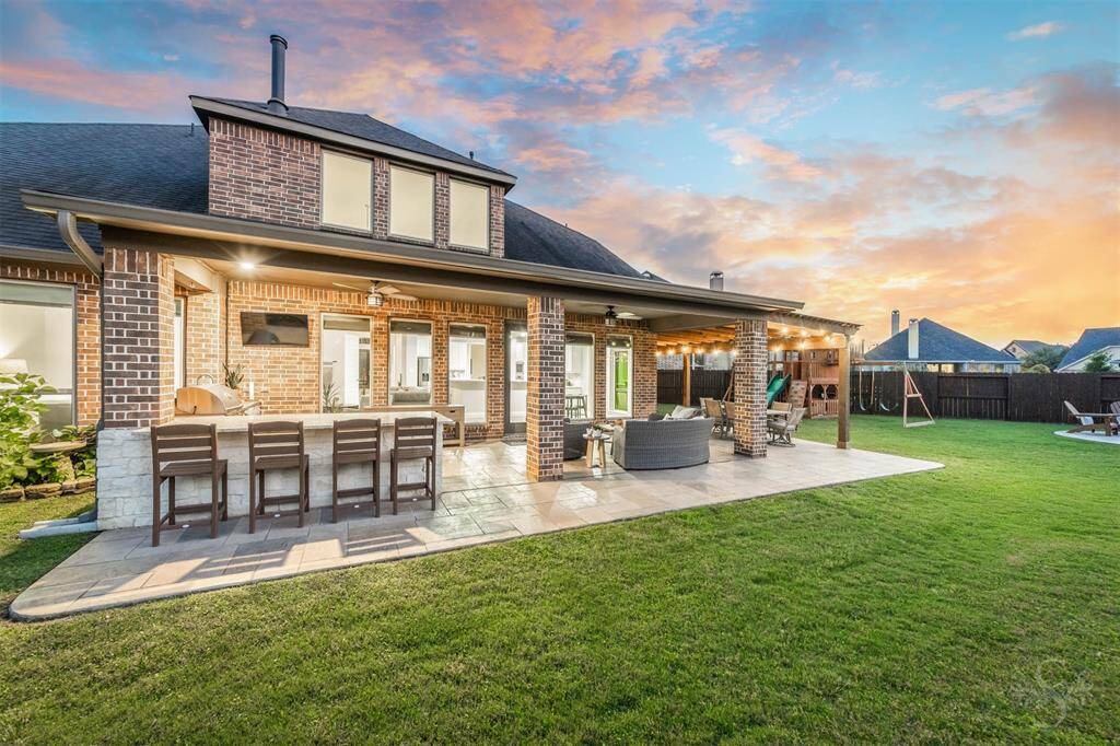 Imagine spending your evenings at this incredible outdoor living area features an extended covered patio with elegant columns, built-in outdoor kitchen, bar seating, and plenty of room for dining and lounging furniture. Surrounded by a pool-sized lush back yard, this space is perfect for elevated entertaining.