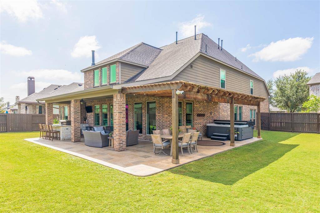 Magnificent outdoor living area features an extended covered patio with elegant columns, built-in outdoor kitchen, bar seating, and plenty of room for dining and lounging furniture. Surrounded by a pool-sized lush back yard, this space is perfect for elevated entertaining.