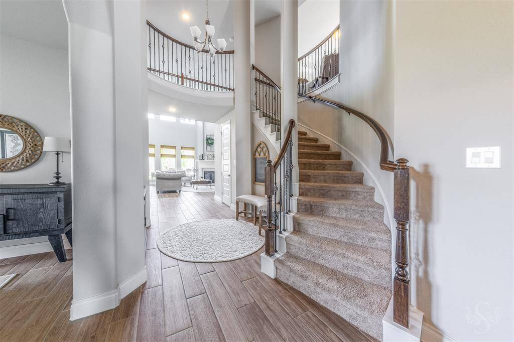 An elegant curved staircase with wrought iron balusters and wood railings creates a striking architectural focal point. The view from the living room highlights the home’s grand scale and open design.