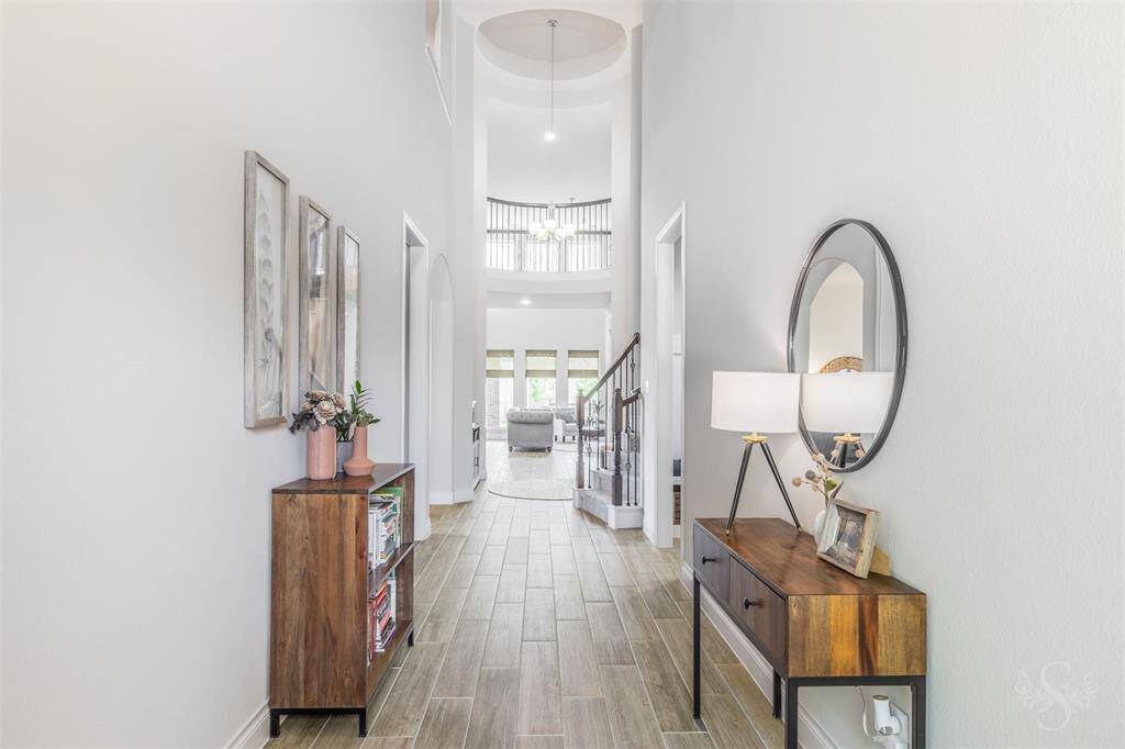 A stunning rotunda ceiling and curved staircase create a dramatic entry, complemented by elegant tile floors and natural light. The view leads directly into the open living space, offering a welcoming first impression.