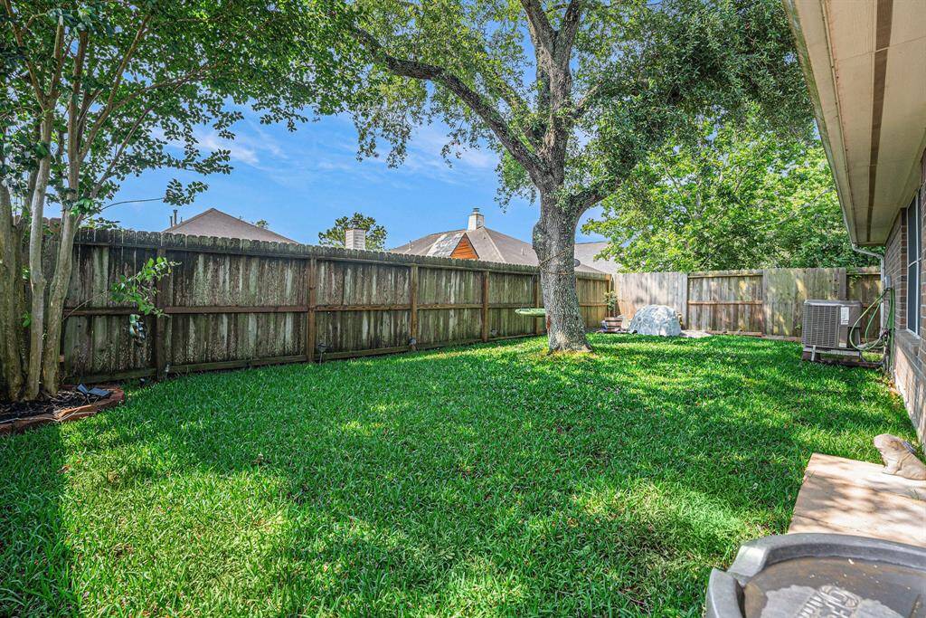 This photo shows a spacious backyard with lush green grass, a large tree providing shade, and a wooden fence for privacy. Ideal for outdoor activities and relaxation.