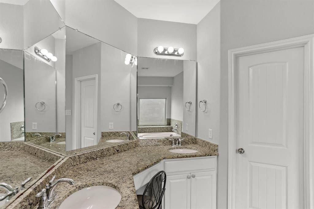 This Primary bathroom is complete with large mirrors, a vanity area, double sinks, granite countertops and backsplash.