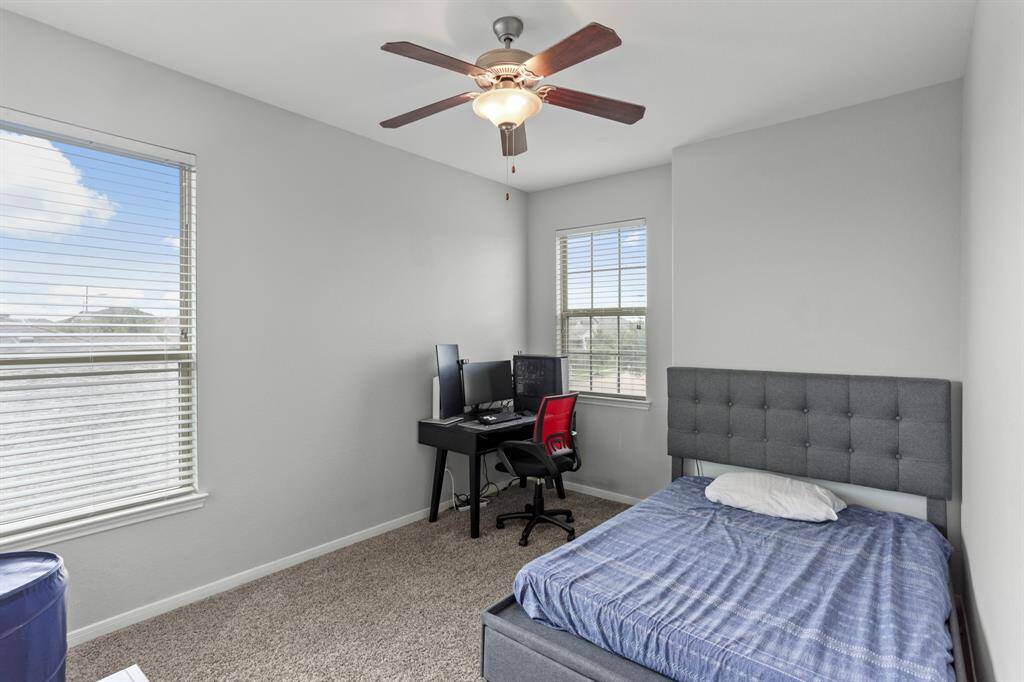 Bright and airy secondary bedroom with neutral paint, plush carpet, a ceiling fan, and windows with privacy blinds.