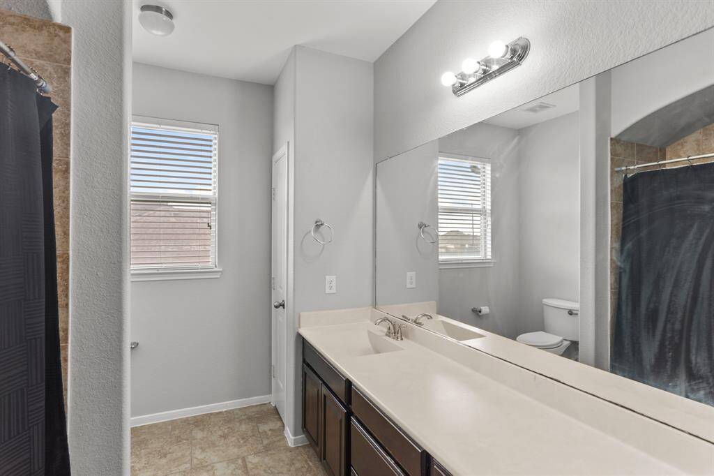 Lovely secondary bathroom complete with a large mirror, granite countertops and wooden cabinets, and a shower/tub combo with a gorgeous tile shower wall.