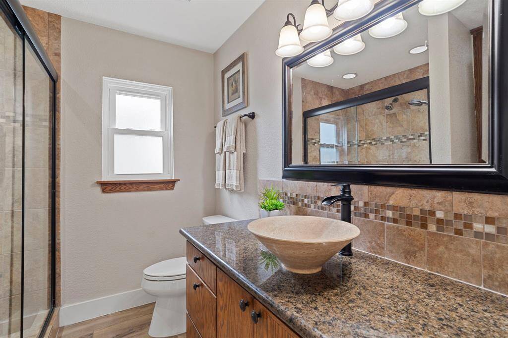 The en suite primary bathroom offers a touch of luxury with a large vanity topped with granite, a stylish vessel sink, and a sleek walk-in shower—creating a spa-like retreat right at home.