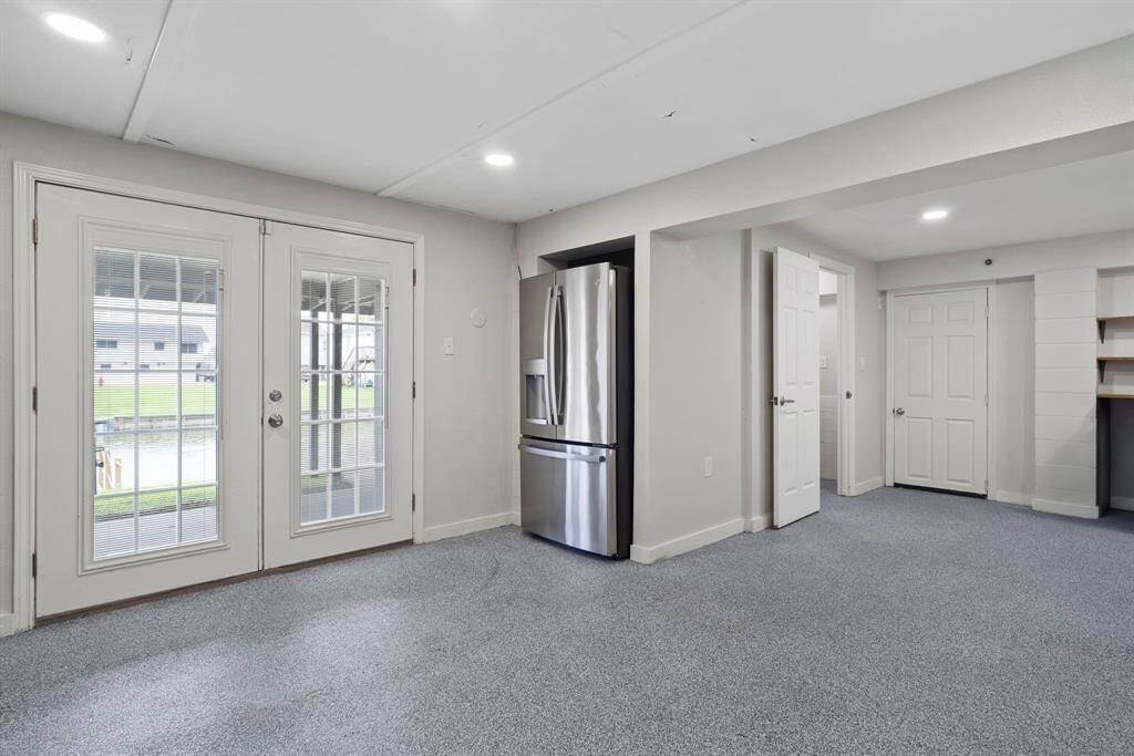 Spacious game room features recessed lighting, epoxy concrete flooring, built-in cabinetry, a half bathroom, and French doors that open to a patio overlooking the water.