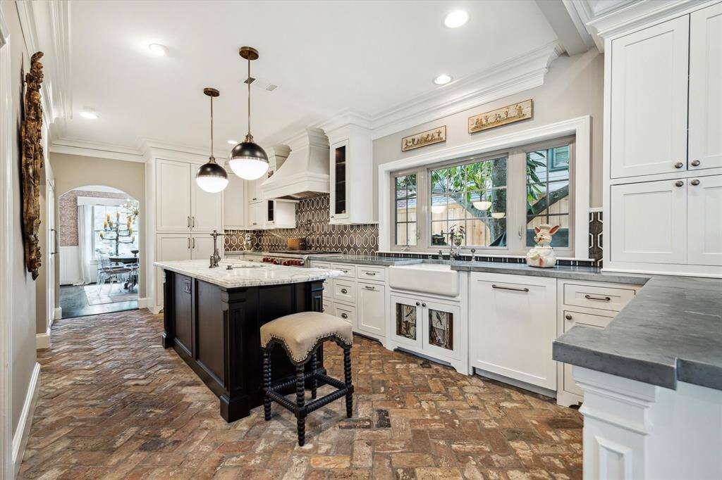 Anchored by antique brick flooring and a dramatic range hood, this open-concept kitchen features Wolf and Sub-Zero appliances, a statement island, and bespoke marble and zinc countertops.