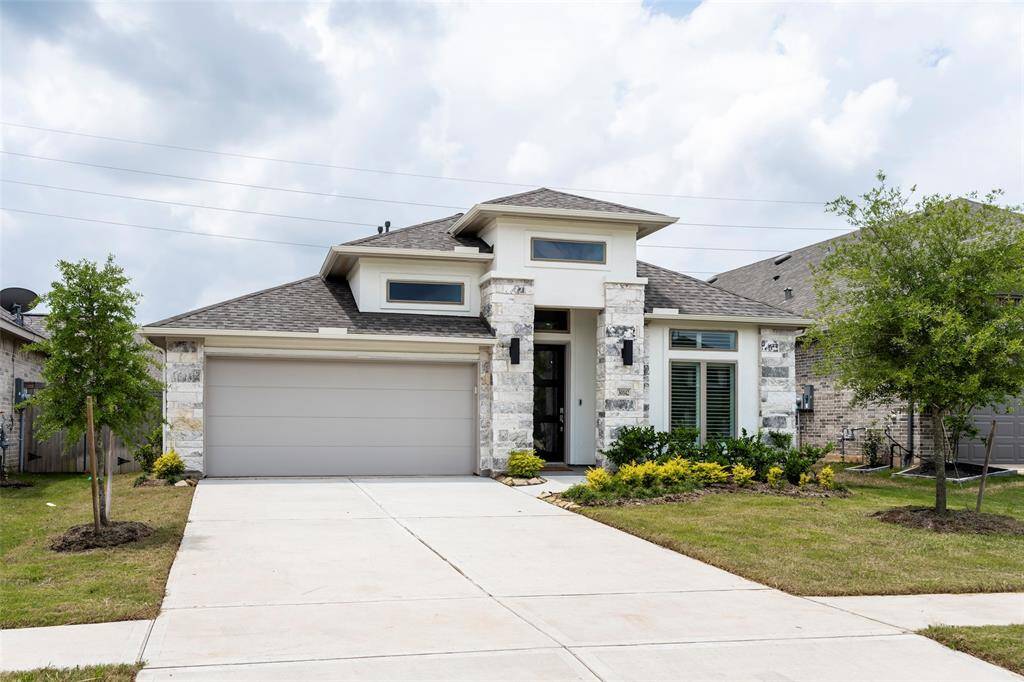 This modern single-story home features a clean, stone facade with a spacious two-car garage. The well-maintained front yard includes manicured shrubs and young trees, offering great curb appeal. Ideal for contemporary living.