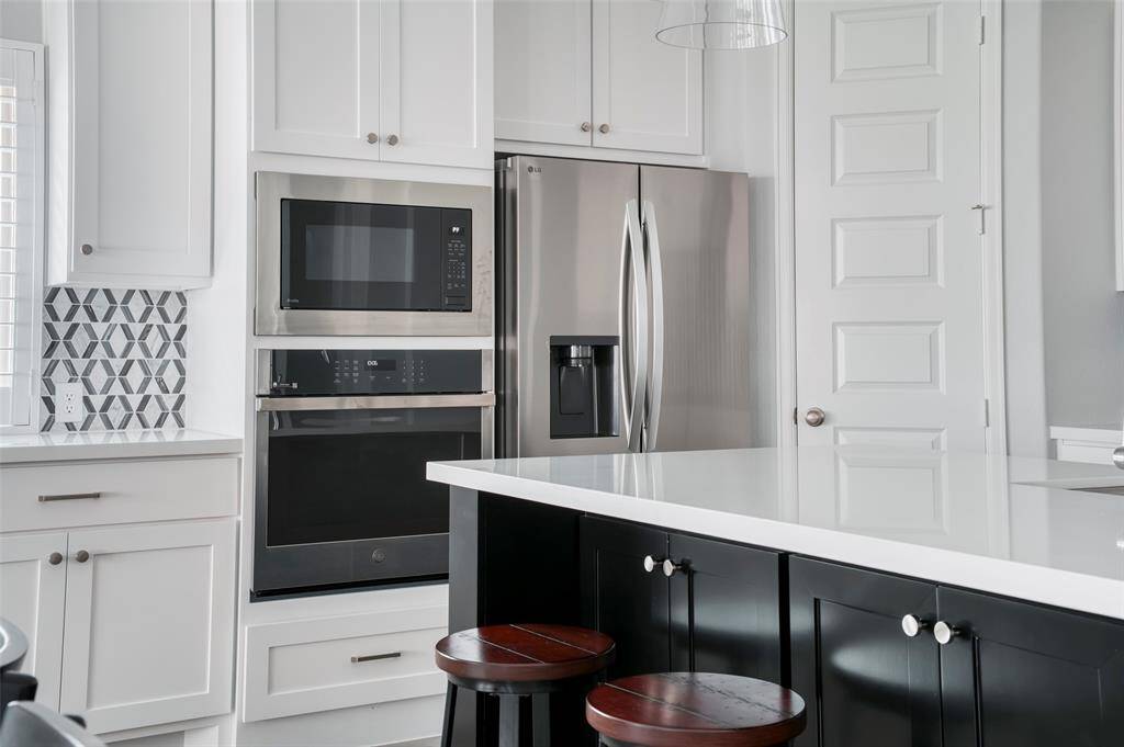 This modern kitchen features sleek white cabinetry, stainless steel appliances including a double oven and fridge, a stylish geometric backsplash, and a spacious island with seating, perfect for entertaining.