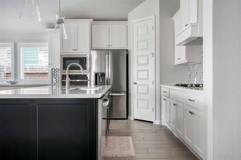 This modern kitchen features sleek white cabinetry, stainless steel appliances, and a stylish backsplash. The island offers ample counter space with a contemporary faucet, while large windows provide natural light. Ideal for cooking and entertaining.