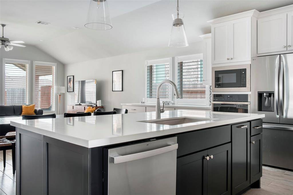 This photo showcases a modern, open-concept kitchen and living area. It features a large island with a sleek sink, stainless steel appliances, and ample cabinetry. The space is bright with natural light from multiple windows, and there's a cozy seating area with contemporary furnishings.