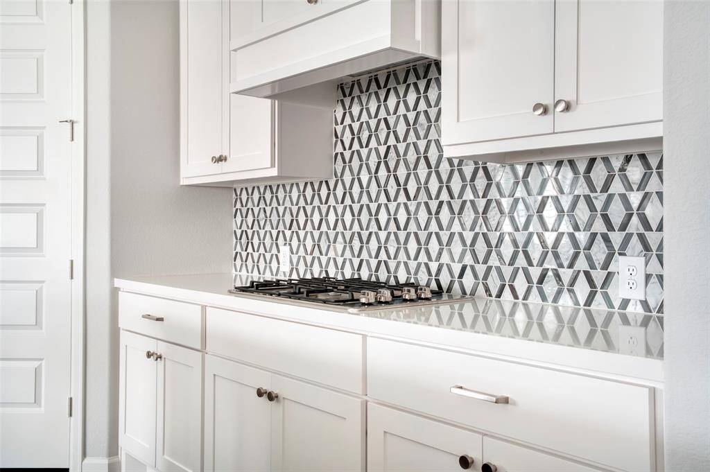 Modern kitchen with sleek white cabinetry and a stylish geometric tile backsplash. It features a built-in gas cooktop and ample storage space, creating a clean and contemporary look.