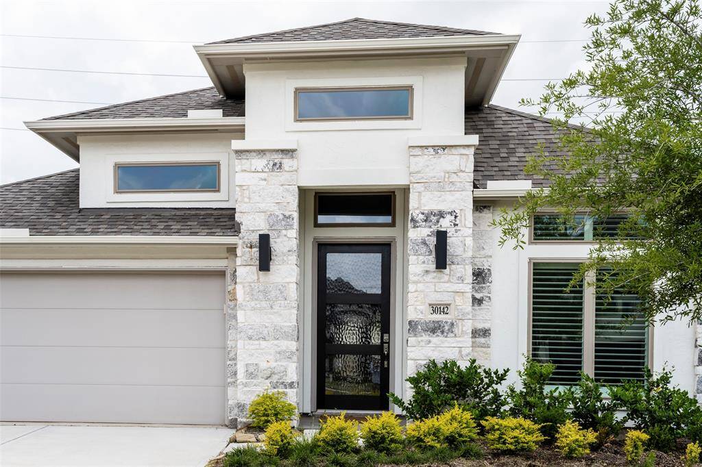 Modern home with a clean facade, featuring a stone accent wall and contemporary front door. It has a sleek garage, well-maintained landscaping, and large windows for natural light.