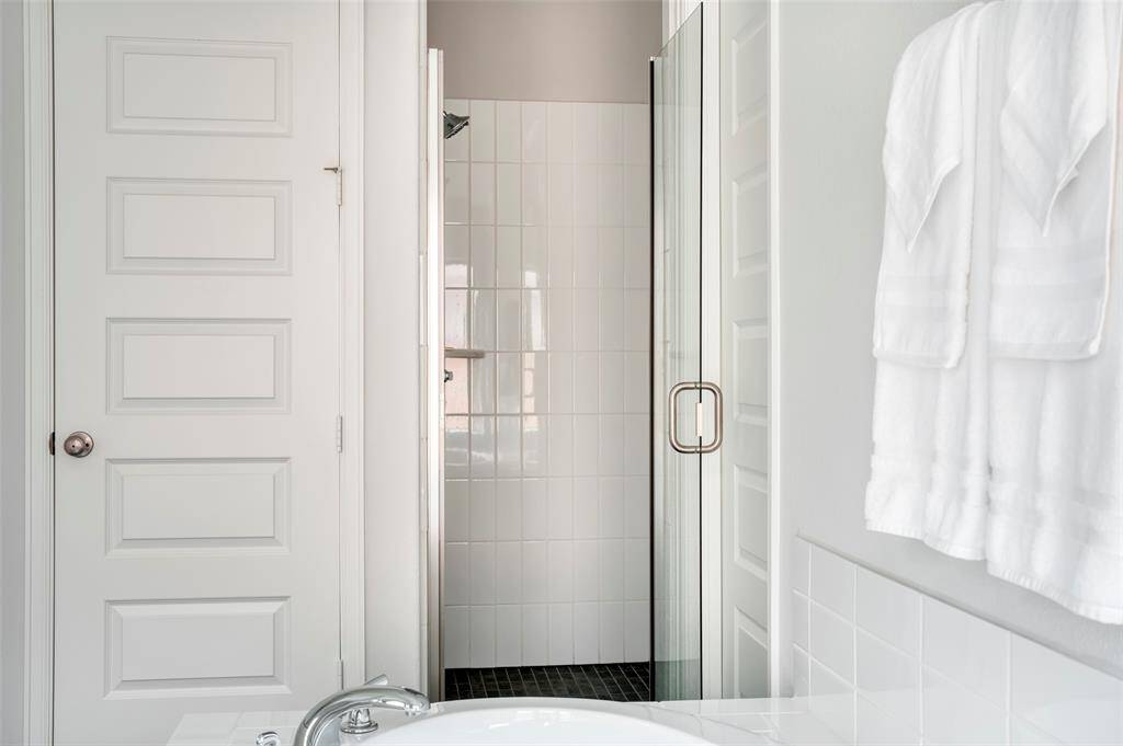 This bathroom features a modern design with a glass-enclosed shower, white tiled walls, and neatly hung towels, offering a clean and inviting space.