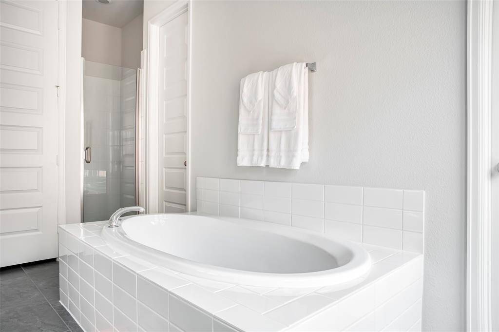 This bathroom features a modern, bright design with a sleek white bathtub, tiled surround, glass-enclosed shower, and soft gray walls, creating a relaxing and inviting atmosphere.
