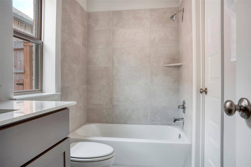 Bright bathroom with a large window, featuring a bathtub and shower, beige tiled walls, and a sleek countertop.