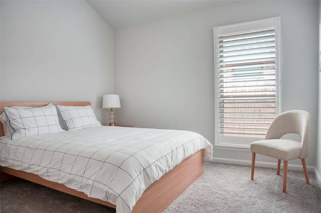 This bedroom features a cozy, minimalist design with a comfortable bed, soft carpeting, and a large window with shutters for natural light. Ideal for relaxation.