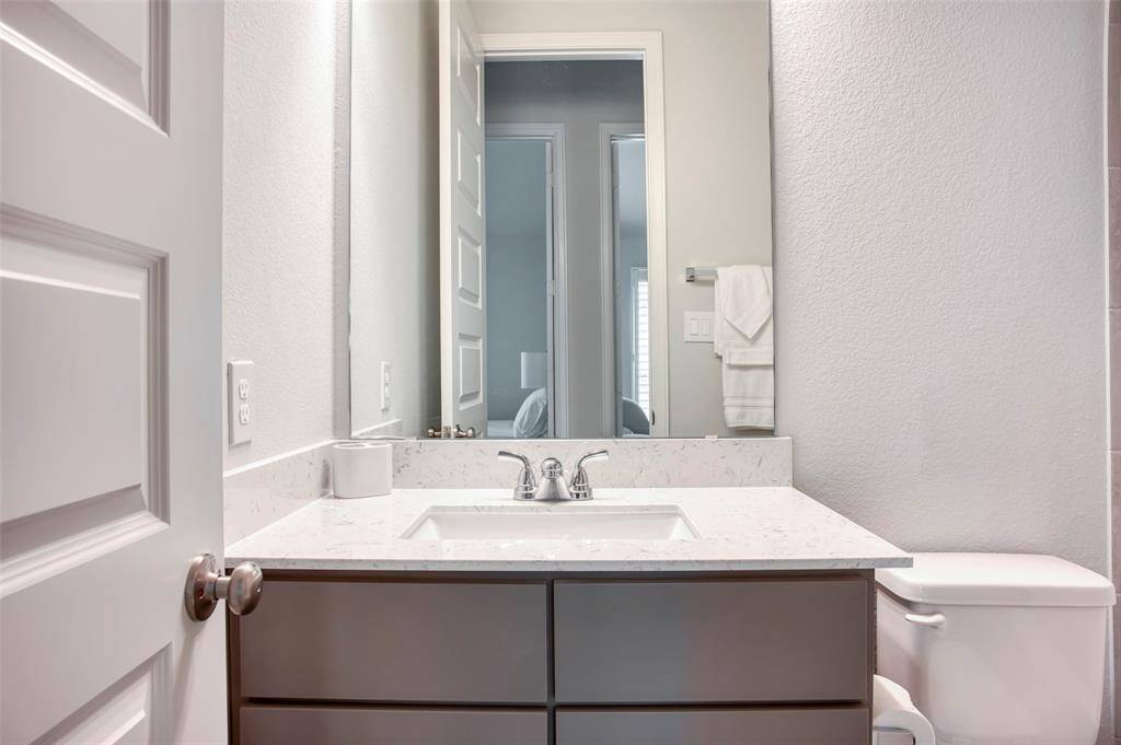 This bathroom features a modern vanity with a sleek marble countertop and an under-mount sink. It includes a large mirror, neutral wall color, and a convenient toilet, offering a clean and bright space.