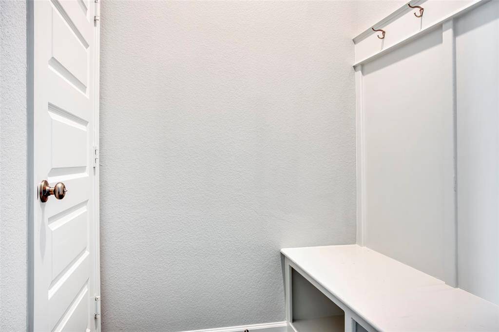 This photo shows a small mudroom area with a simple white bench and coat hooks above, adjacent to a white door.