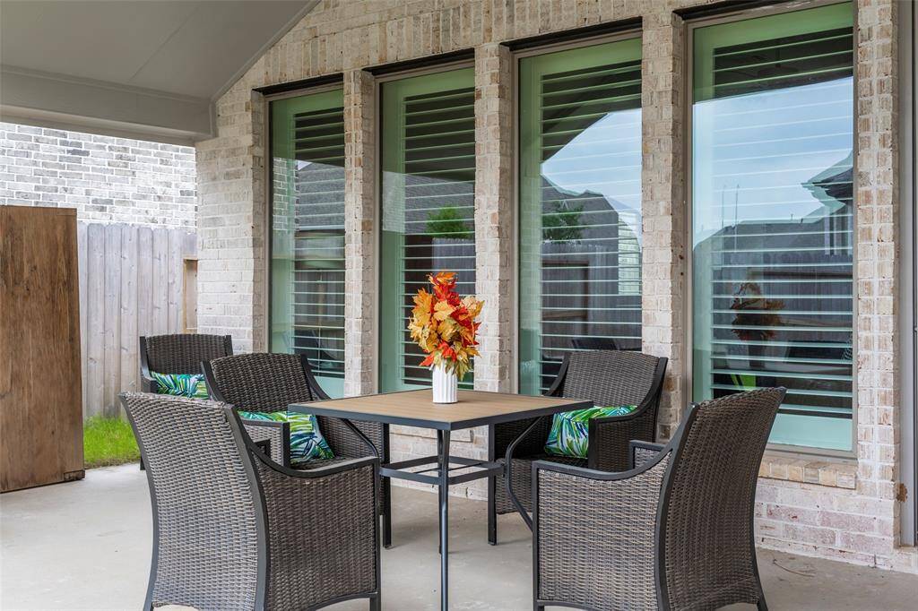 This photo showcases a cozy, covered patio with a table and four wicker chairs, perfect for outdoor dining. Large windows provide a view into the home, and a wooden fence offers privacy.