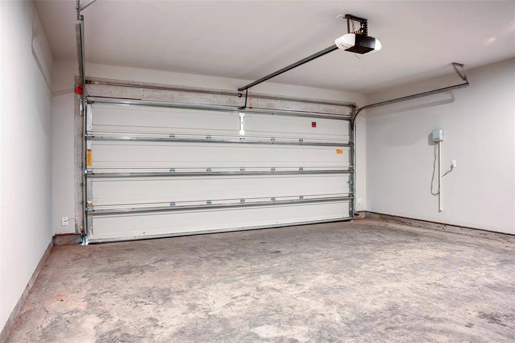 This photo shows a spacious, clean garage with a white automatic door, concrete flooring, and ample space for vehicle storage or a workshop area.