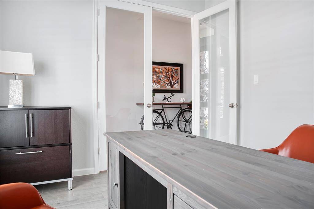 Modern home office with glass double doors, stylish dark furniture, and bright orange chairs. A decorative bike and artwork add charm to the space, offering a blend of functionality and aesthetics.