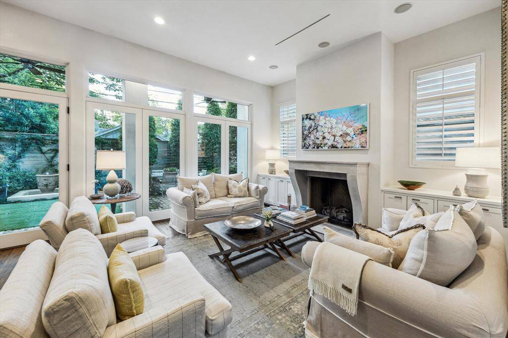 Living room with honed stone fireplace, custom built-ins, and floor-to-ceiling windows overlooking the private courtyard.