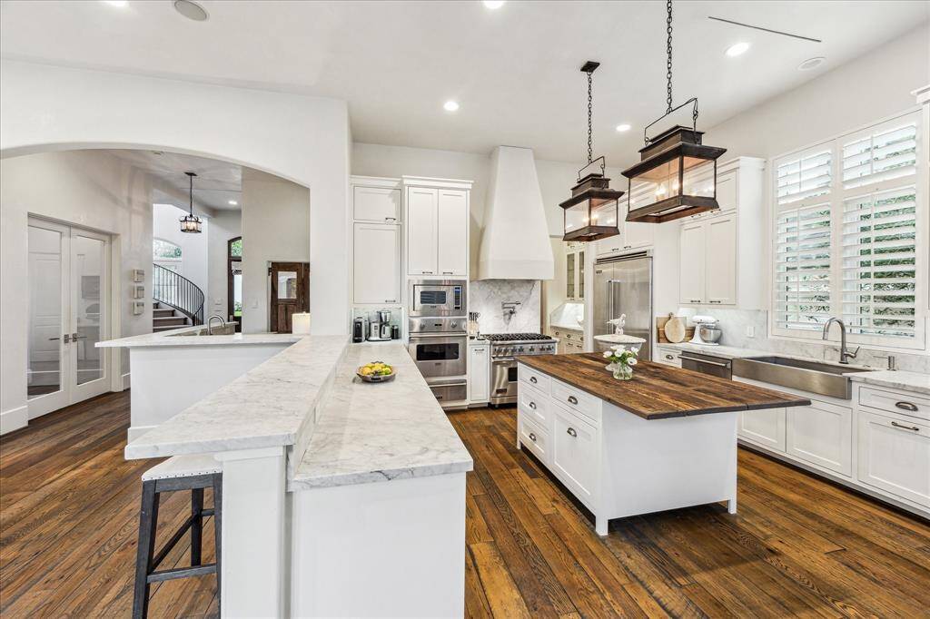 Kitchen view with Viking range, pot filler, Carrera marble, and antique wood island—anchored by two statement lanterns and open sightlines.
