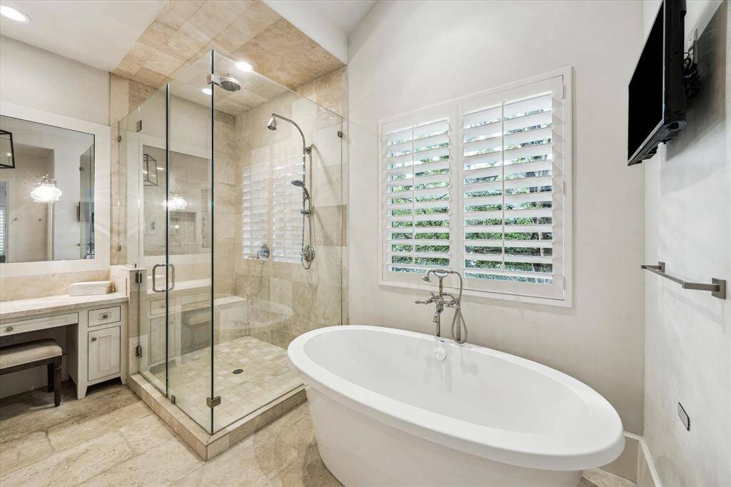 Primary bath features soaking tub, frameless shower, and natural light through privacy-shaded windows.