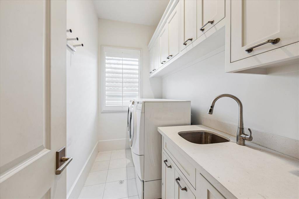 Spacious laundry room with built-in sink, abundant cabinetry, and natural light through plantation shutters.