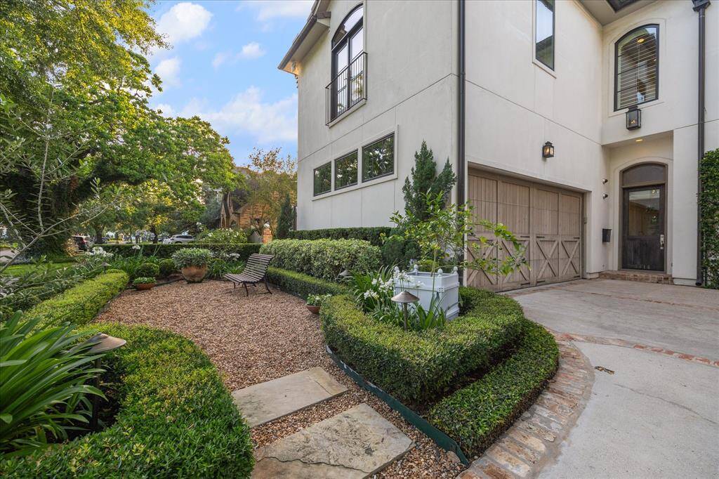 Large two-car garage with cobblestone border, surrounded by lush formal landscaping and a charming gravel courtyard.