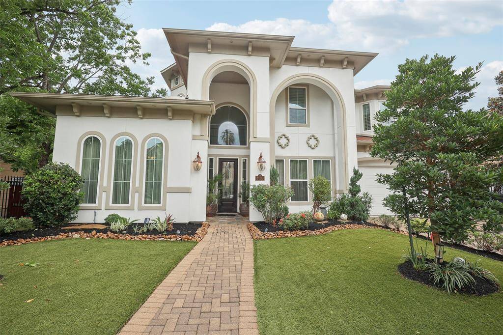 The property is enclosed by a wrought-iron fence and features a spacious driveway. The sunset sky adds a warm, inviting backdrop.