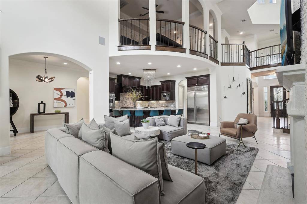 This spacious living area features high ceilings and an open floor plan with a view of the kitchen. It includes a modern, comfortable seating area, elegant decor, and a stylish staircase leading to the upper level. Perfect for entertaining and family gatherings.