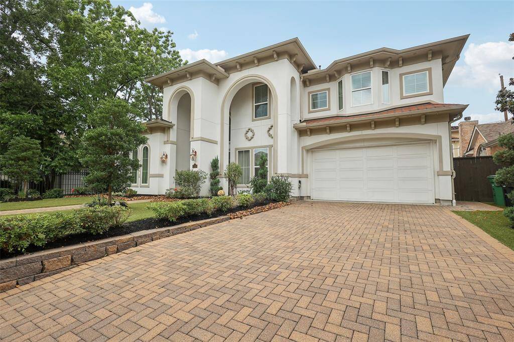 This elegant two-story home features a Mediterranean-inspired facade with arched windows and a welcoming central entrance. The well-maintained landscaping includes lush greenery and a paved walkway leading to the front door, creating an inviting and stylish exterior.
