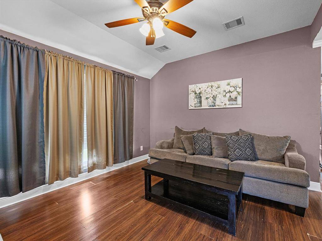 Living room with hardwood floors, ceiling fan and large windows to allow natural light.