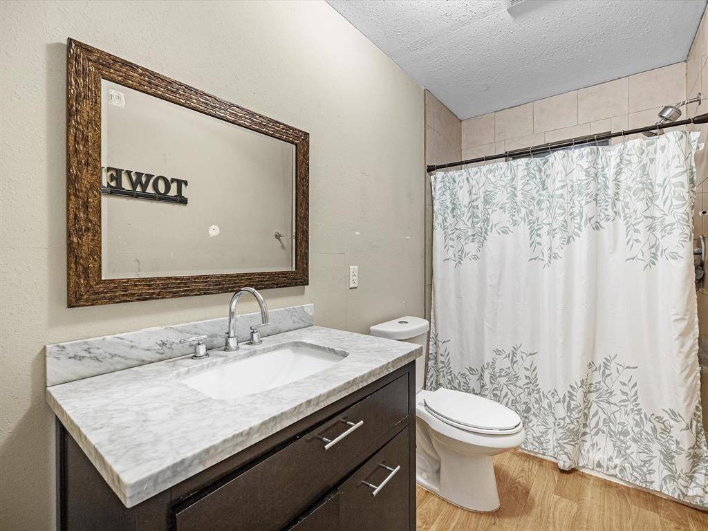 This bathroom features a modern vanity with a marble countertop, a large framed mirror, and shower. It has a clean, neutral color palette and wood-like flooring.