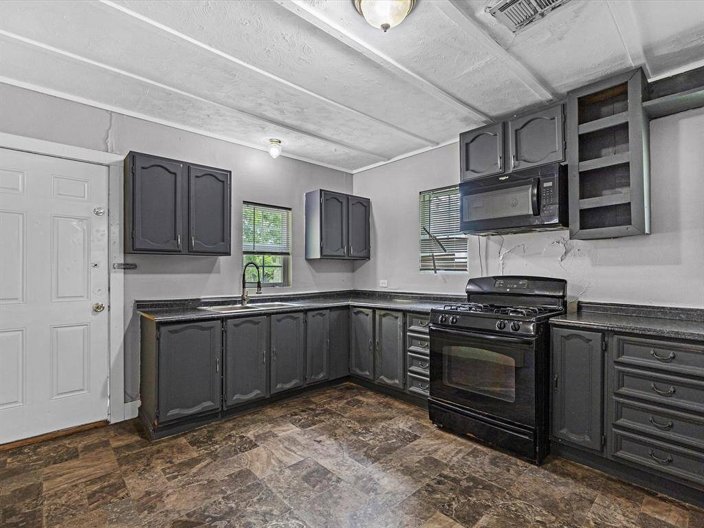 This kitchen features dark cabinetry with a black stove and microwave, providing a sleek look. It has ample counter space, multiple windows for natural light, and a durable tile floor.