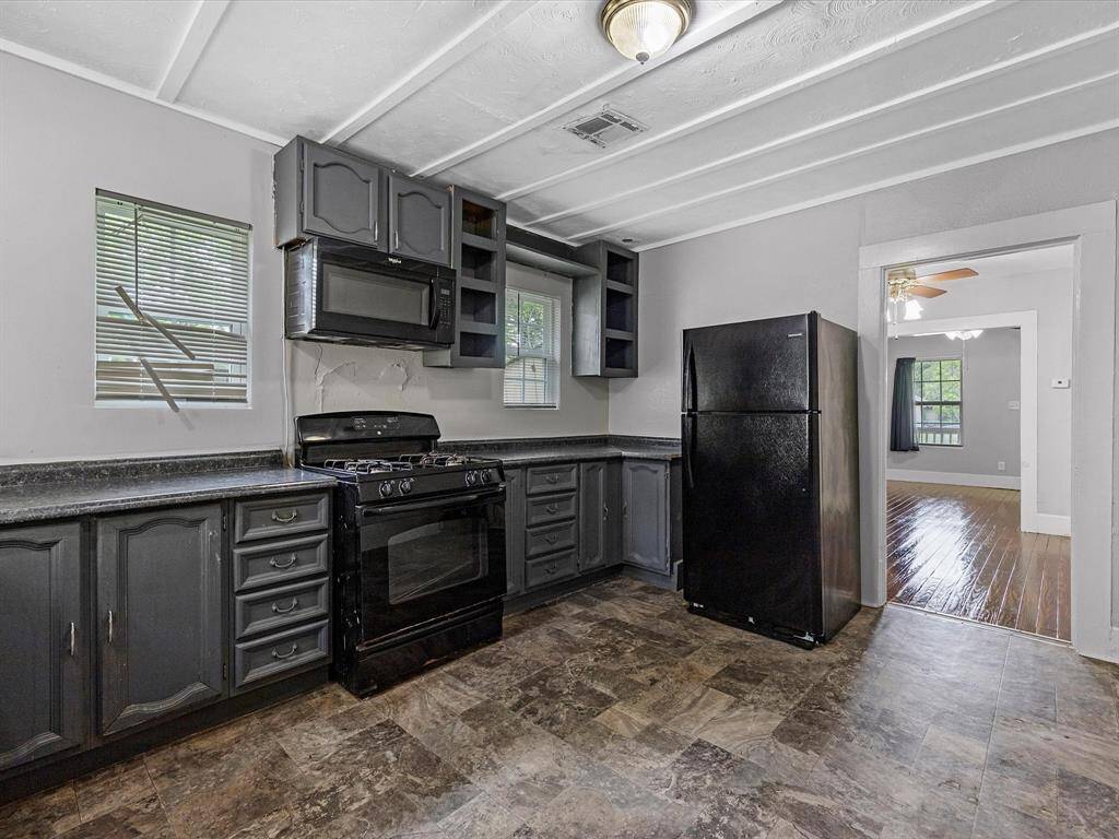 This kitchen features dark cabinetry with a black stove and microwave, and fridge providing a sleek look. It has ample counter space, multiple windows for natural light, and a durable tile floor.