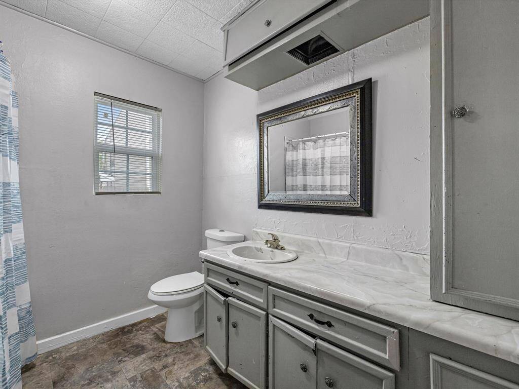 This bathroom features a classic design with a single sink vanity, marble countertop, and ample cabinet space. It includes a window for natural light and shower.