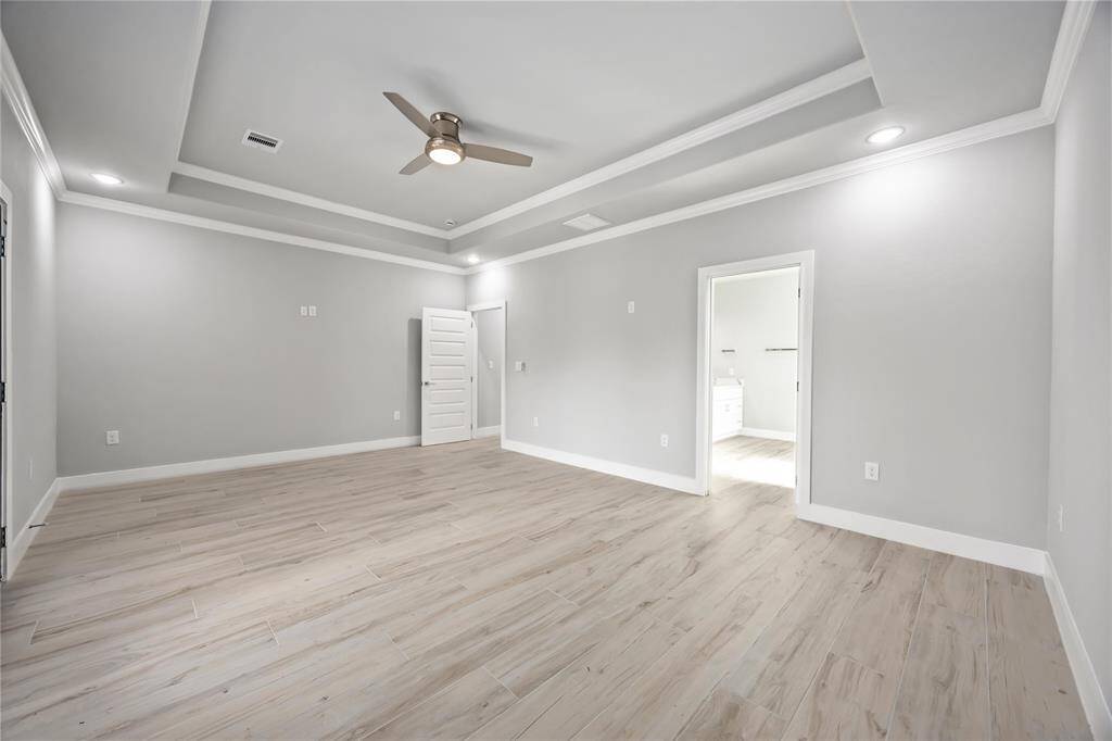 Serene owner's sanctuary features sophisticated coffered ceiling detail, premium flooring, and elegant French doors opening to a private balcony