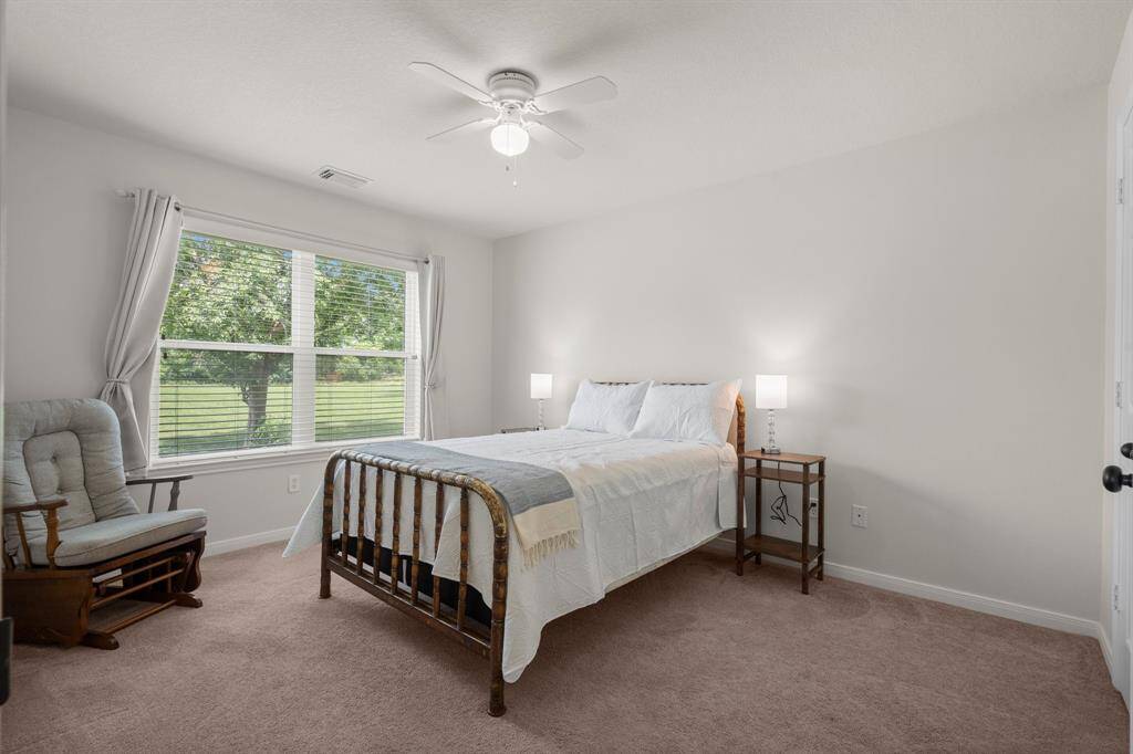 This cozy bedroom provides a comfortable retreat with a ceiling fan and a large window that brings in natural light and offers views of the surrounding greenery.