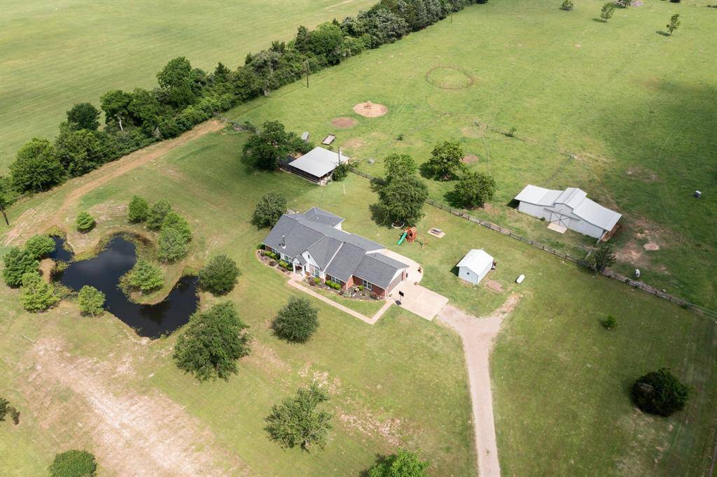 This aerial perspective reveals the unique layout of this property, featuring a charming home, a tranquil pond, and various outbuildings, all nestled within a vast expanse of land. Enjoy the peaceful setting and the endless possibilities this property offers.