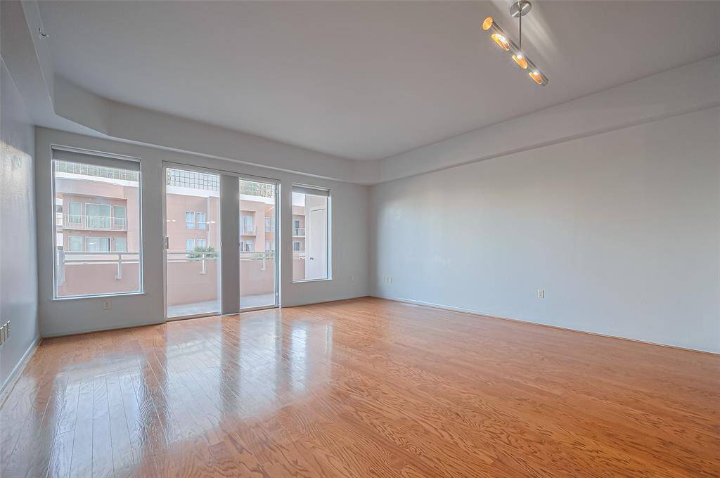 Bright, spacious room with hardwood floors, large windows, and a modern light fixture, offering a view of a neighboring building. Ideal for living or dining area.