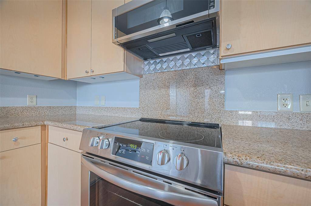 Modern kitchen with stainless steel appliances, sleek electric stove, and built-in microwave. It features light wood cabinetry and granite countertops, offering a clean and contemporary look.